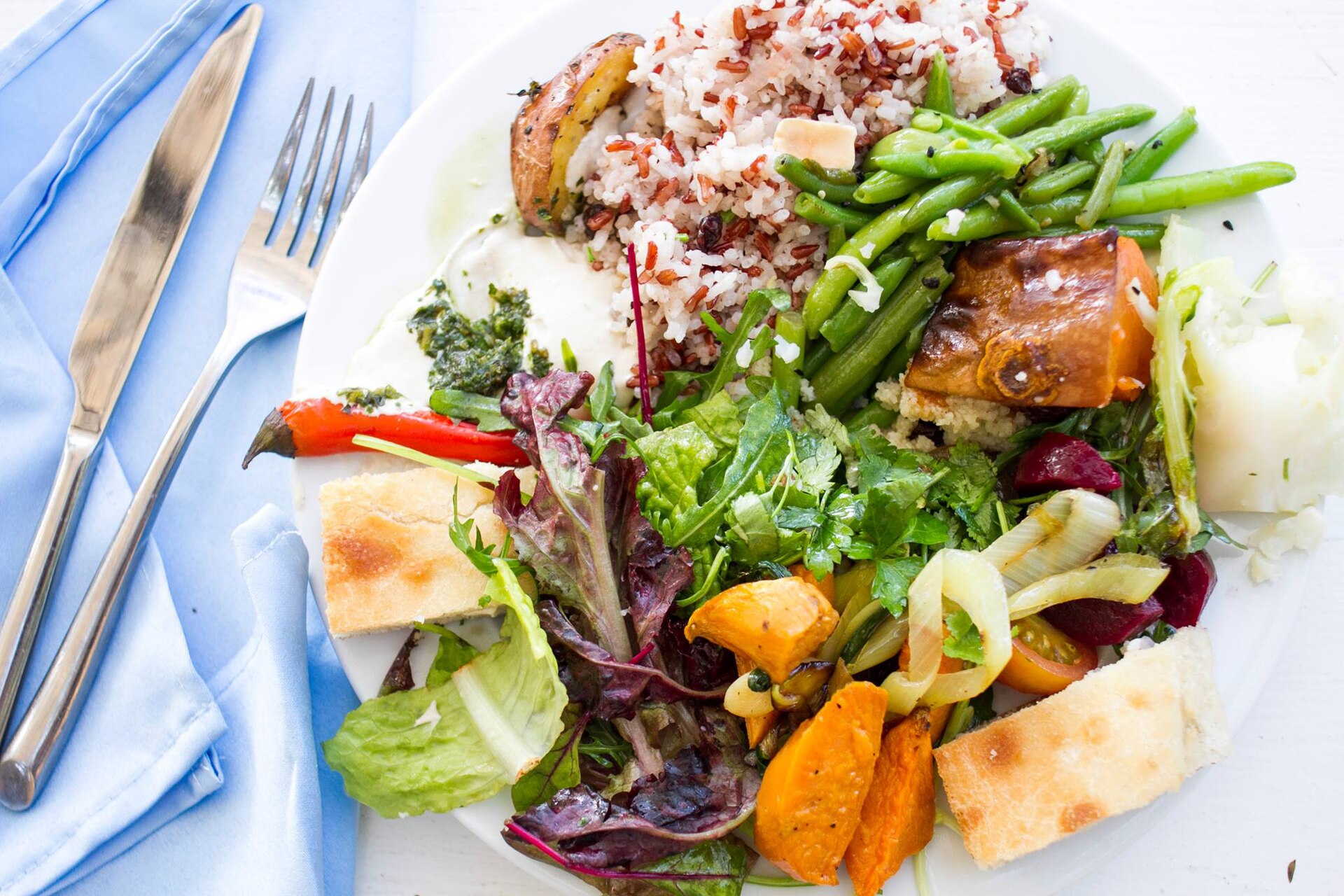 Vegan plate of mixed salad leaves, roasted squash and beetroot, green beans, red and white rice, tahini with green herb sauce and flatbread