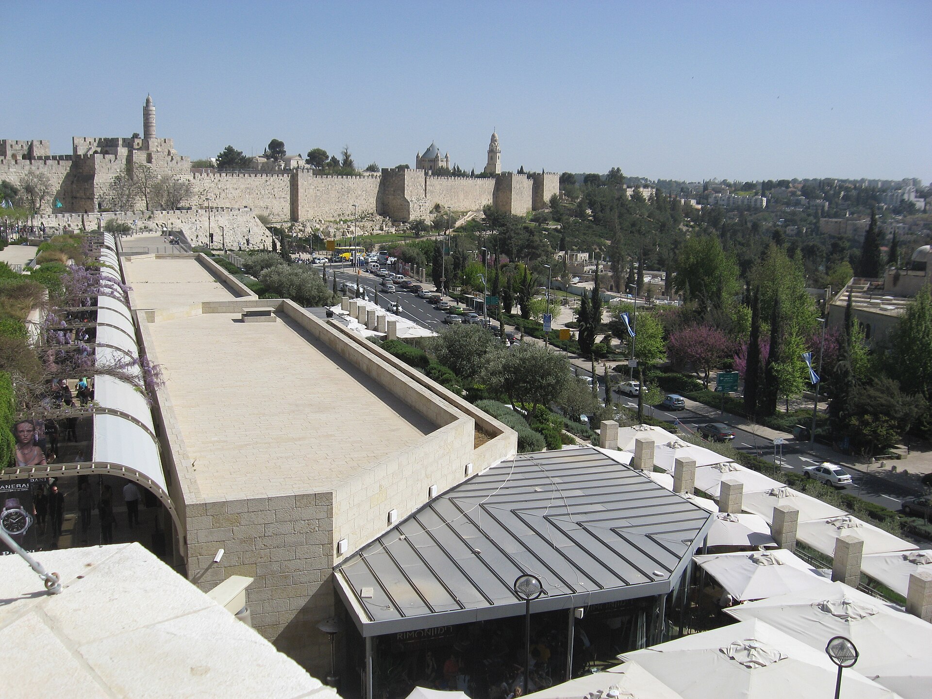 View from the upper level of Mamilla in Jerusalem over café parasols and a road to the Old City walls, the Tower of David and the Dormition Abbey