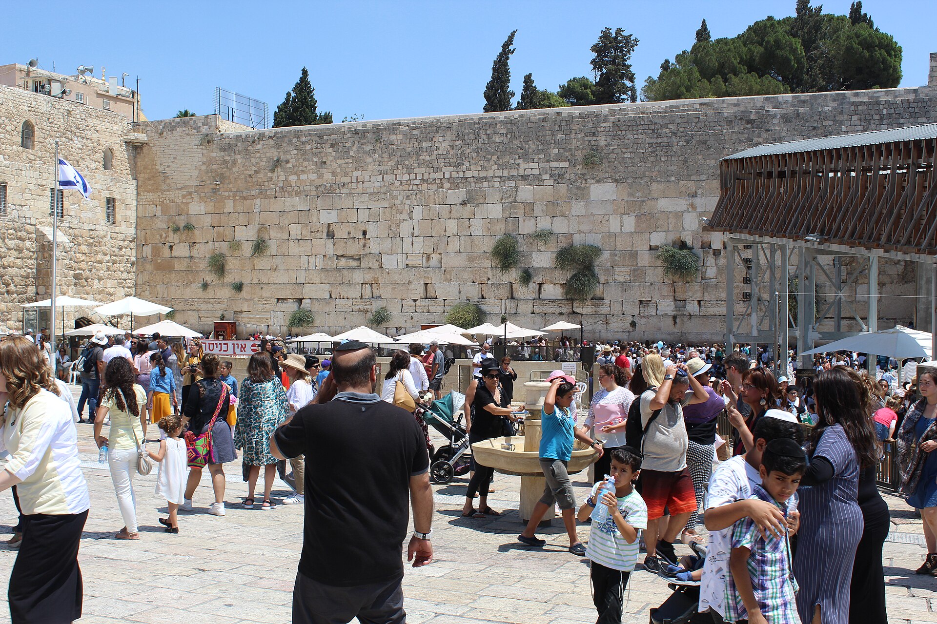 Crowds of visitors, families and children milling around the Western Wall plaza on a sunny day, with the Wall and prayer area behind