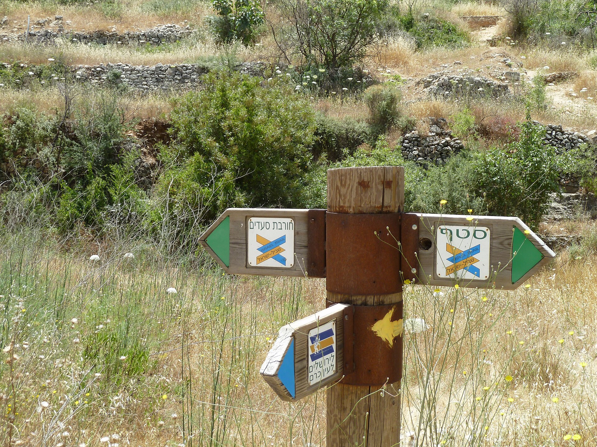 Wooden trail signpost near Ein Kerem with Israel National Trail plaques pointing to Sataf and Horvat Sa'adim and a Jerusalem Trail lion plaque pointing to Jerusalem
