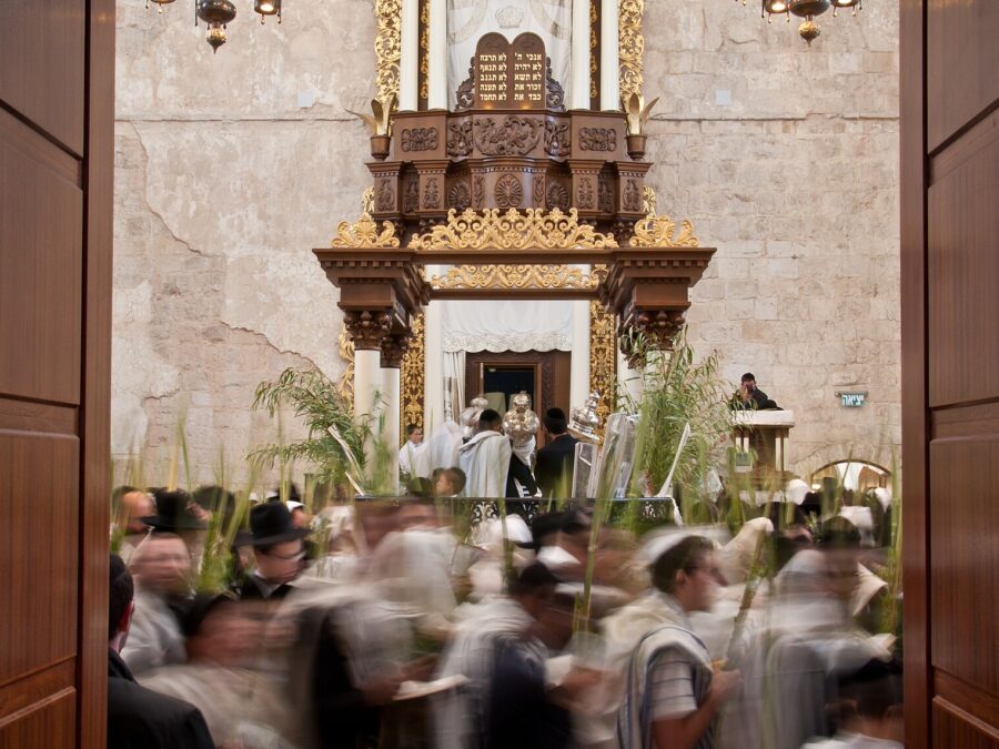 Worshippers in prayer shawls circle with palm-frond lulavim before the gilded Torah ark of the Hurva Synagogue during Hoshana Rabbah, seen through open doors