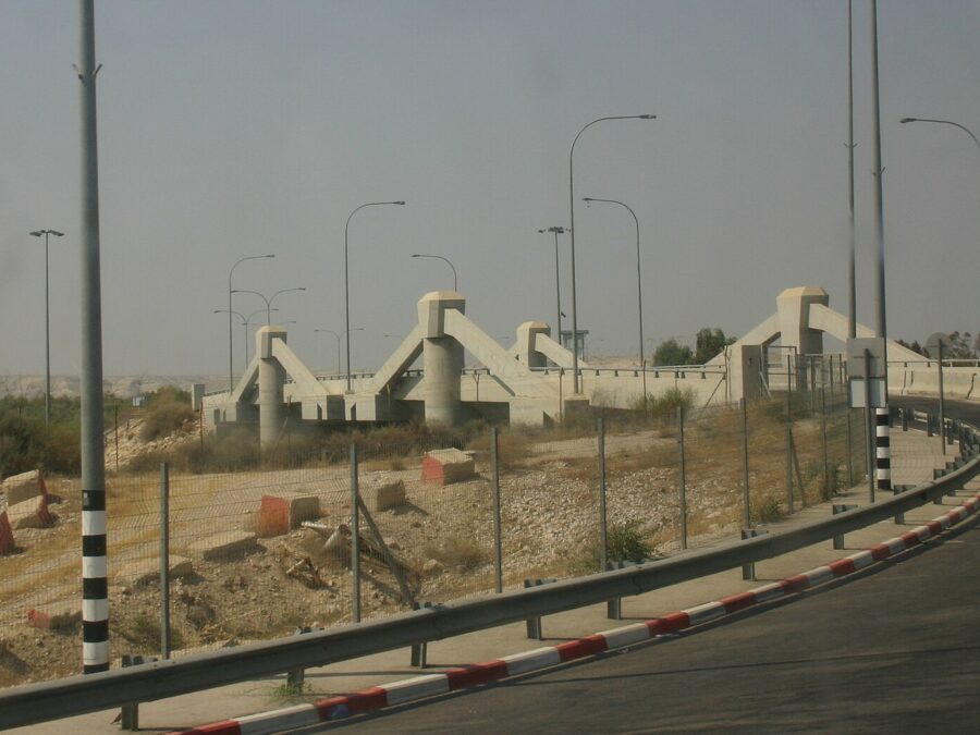 The concrete Allenby / King Hussein Bridge across the Jordan Valley seen from the curving approach road, with a watchtower, fencing and a bus