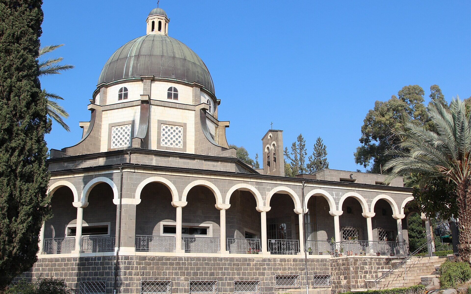 The domed, arcaded Church of the Beatitudes on the Mount of Beatitudes, framed by cypress and palm trees under a blue sky