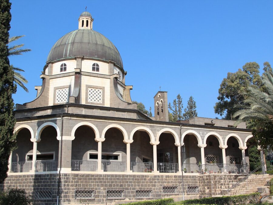 The domed, arcaded Church of the Beatitudes on the Mount of Beatitudes, framed by cypress and palm trees under a blue sky