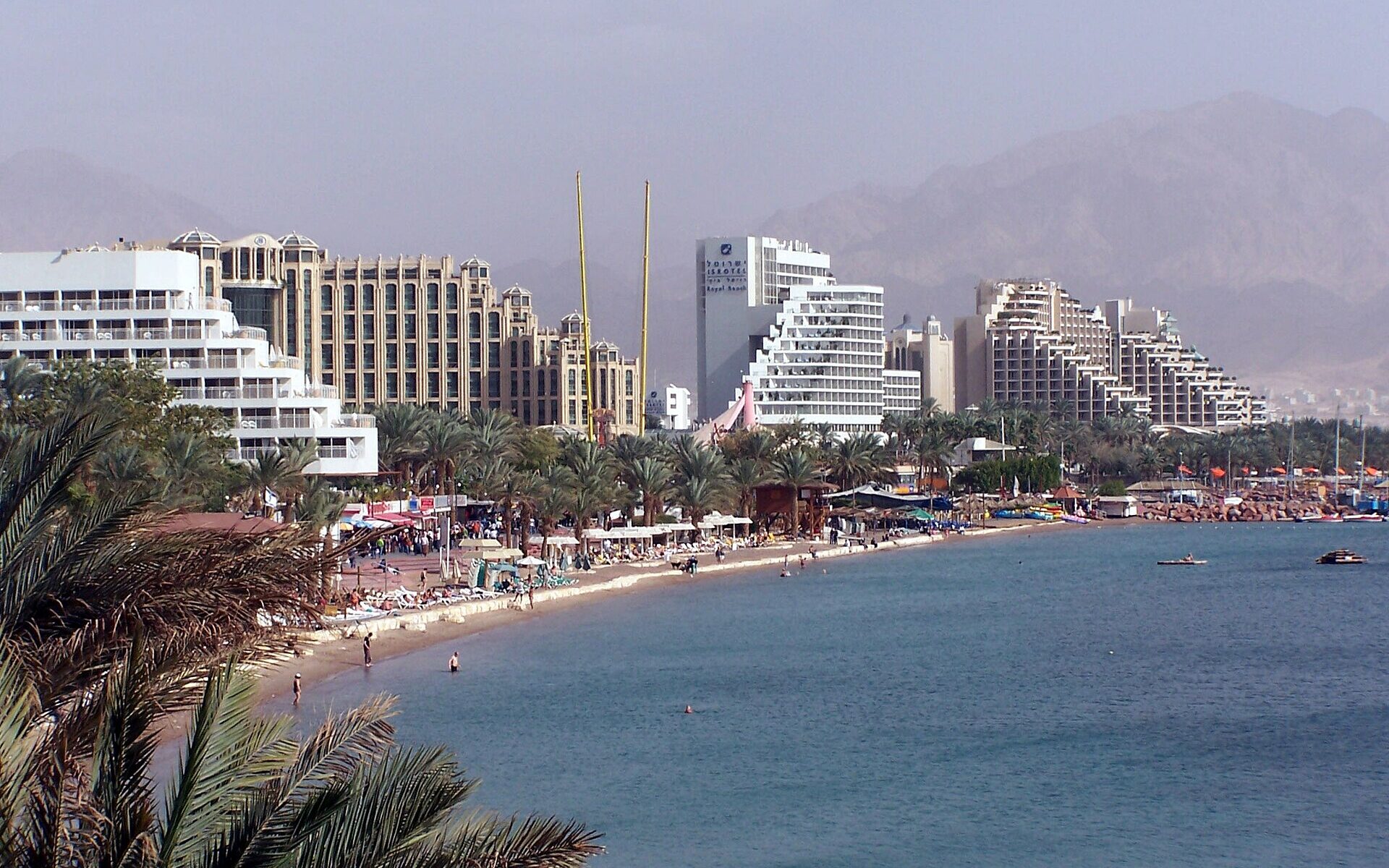Eilat's North Beach lined with large hotels and palm trees on the Gulf of Aqaba, with bare mountains behind