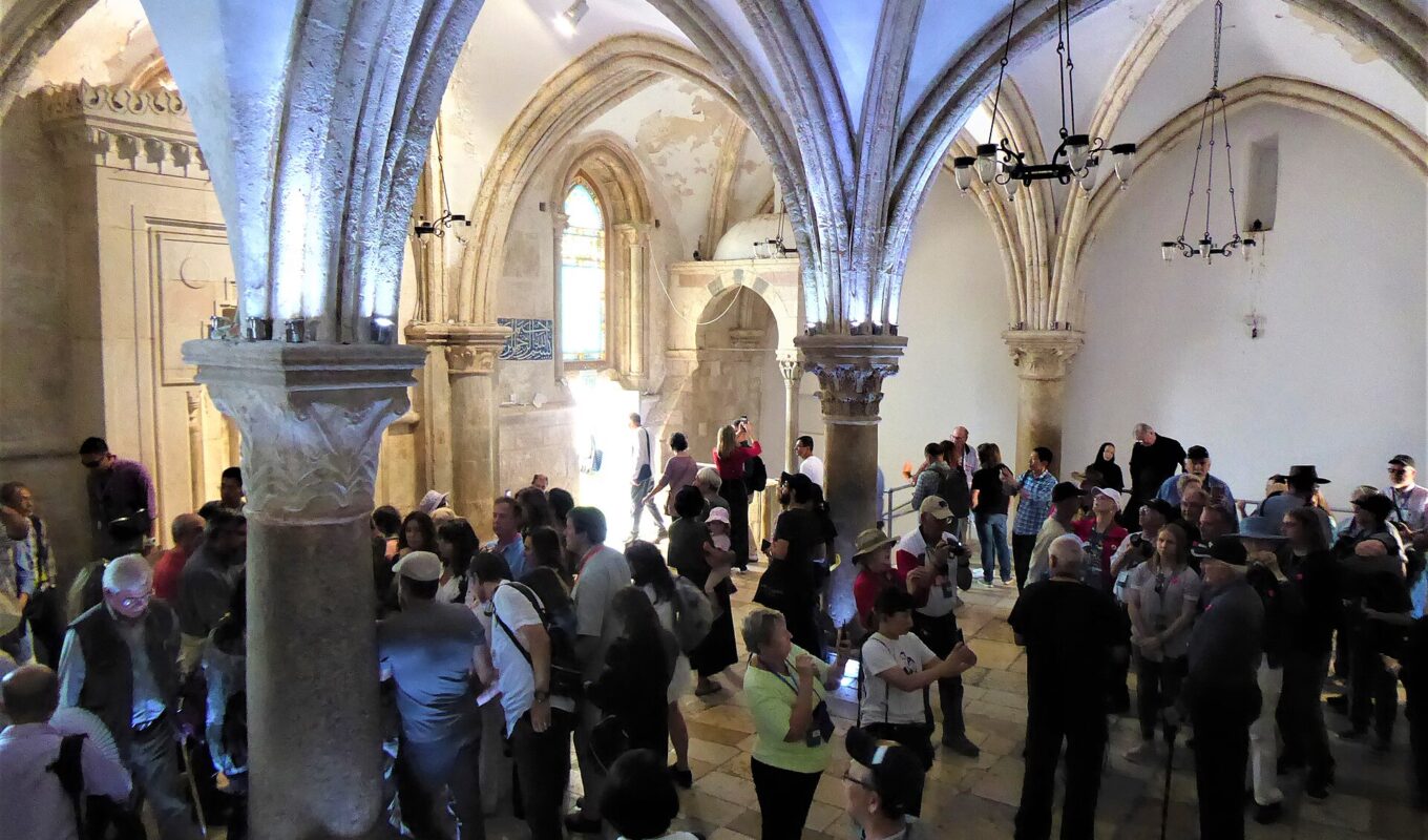 A crowded vaulted Gothic hall with slender columns and ribbed pointed arches, full of visitors standing in groups