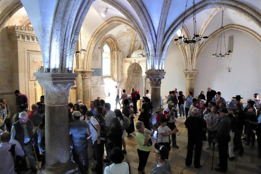 A crowded vaulted Gothic hall with slender columns and ribbed pointed arches, full of visitors standing in groups