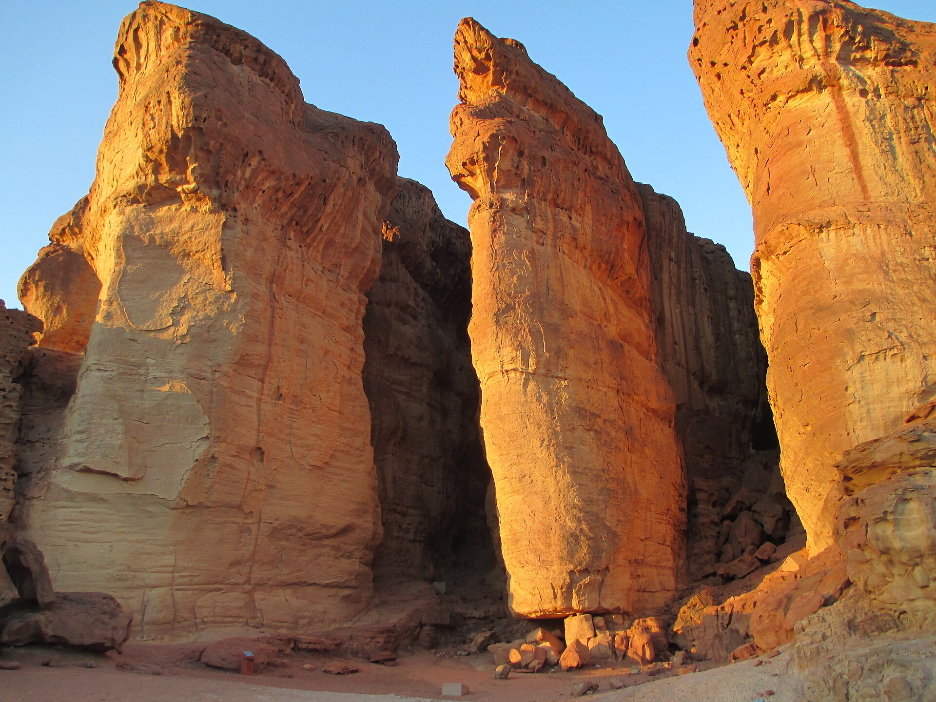 Tall sandstone columns of Solomon's Pillars in Timna Park glowing golden orange in low sunlight against a blue sky